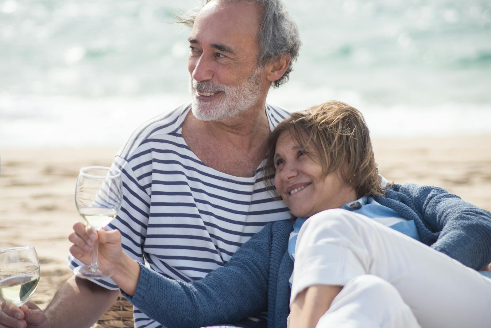 Senior couple smiling and enjoying white wine on a sunny beach in Portugal.