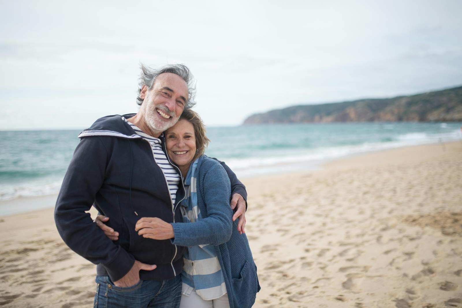 Happy senior couple embracing on a sandy beach in Portugal, symbolizing love and togetherness.