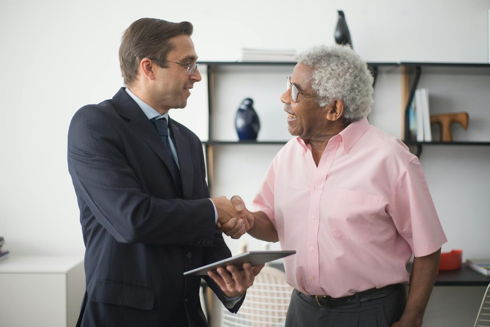 Two businessmen shaking hands during a meeting in a bright office environment.