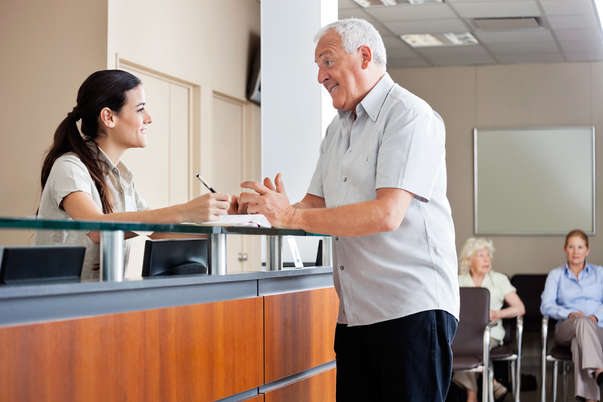 Senior man communicating with female receptionist while women sitting in background